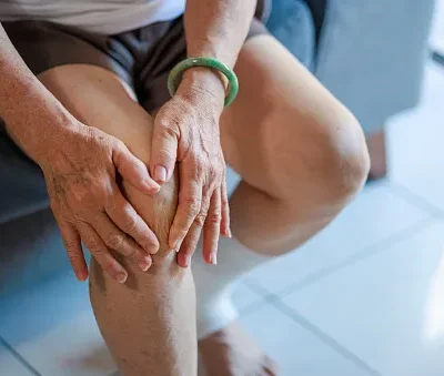 a senior asian woman is massaging her knee while sitting on a sofa in the living room at home